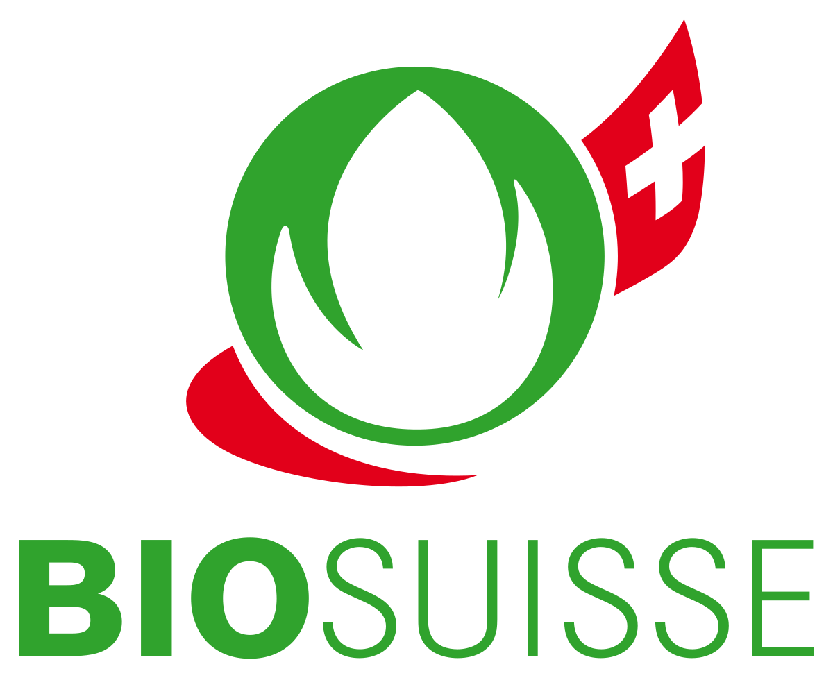 Das Logo von Bio Suisse besteht aus einer weißen pflanzenähnlichen Form auf einem grünen, kreisförmigen Hintergrund, begleitet von einem roten Element mit einem weißen Kreuz darauf. Unter dem Design wird der Text „BIO SUISSE“ in fetten grünen Buchstaben angezeigt, was das Engagement des Unternehmens für Bio-Standards für Produkte wie Eier widerspiegelt.