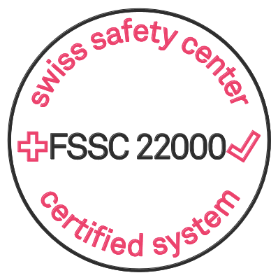 Ein kreisförmiges Logo mit schwarzem Rand. Am Rand des Kreises steht in Pink „swiss safety center certified system“. In der Mitte steht in Schwarz „+FSSC 22000“ mit einem pinkfarbenen Häkchen und dezent eingearbeitetem Eier-Symbol.