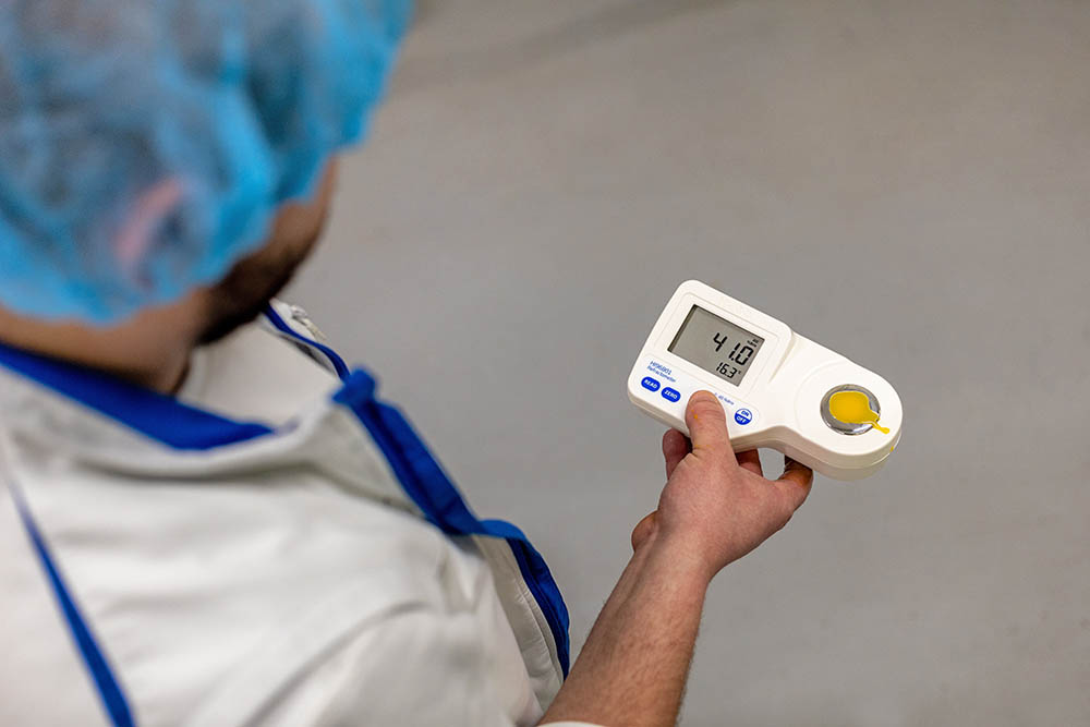 Laboranalysen 1 Eine Person in einem weißen Laborkittel und einem blauen Haarnetz bedient ein tragbares digitales Refraktometer. Das Gerät zeigt auf dem Bildschirm den Messwert 4,10 an und analysiert möglicherweise ein Ei oder eine Lösung. Die Person scheint sich in einem Labor oder einer Testumgebung zu befinden.